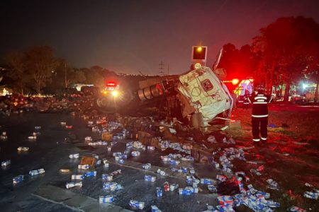 imagem colorida mostra caixas de leite espalhadas por pistas de rodovia e carreta tombada