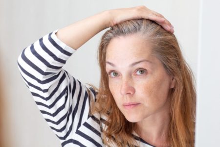 Foto colorida de mulher com a mão no cabelo com fios grisalhos - Metrópoles