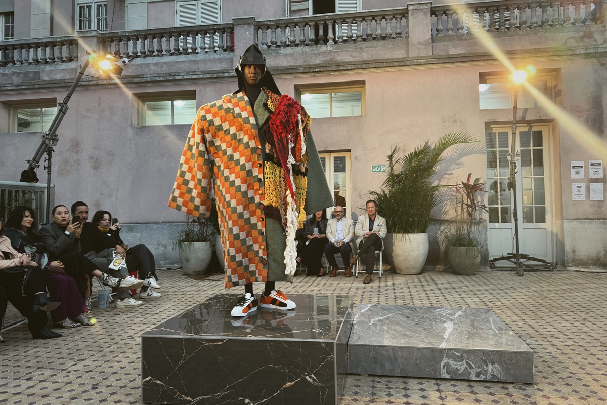 Modelo usa look colorido com retalhos e tricô, em cima de uma base de pedra, em desfile de moda - Metrópoles