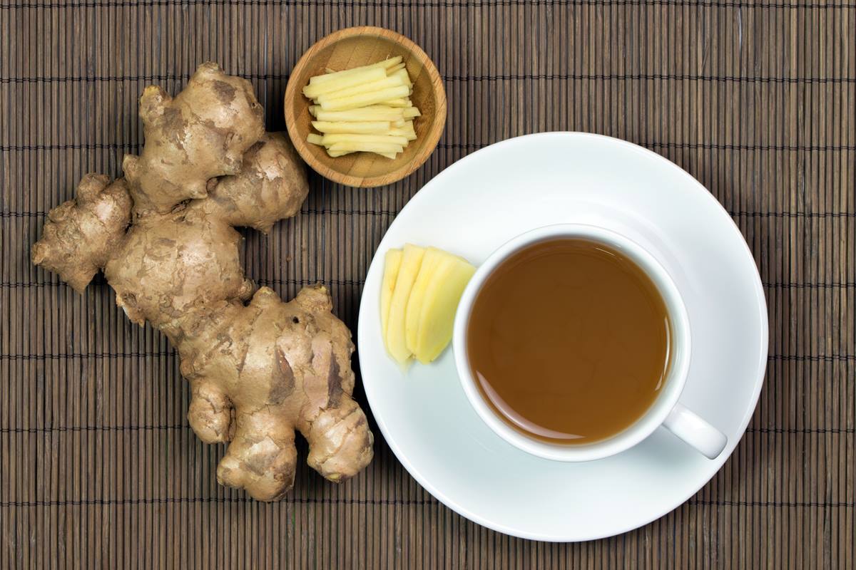 Foto colorida de gengibre, xicara de chá e pedaços da raiz tuberosa dentro de potinho - Metrópoles