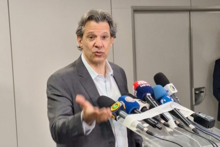 Imagem colorida mostra o ministro da Fazenda Fernando Haddad, um homem branco vestindo um terno cinza e uma camisa branca, diante de um púlpito com microfones de diversas emissoras Senado - Metrópoles
