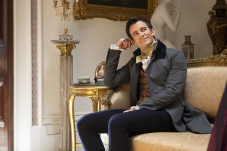 Na imagem colorida, homem está sentado em sofá e sorrindo, com roupa de estilo vitoriano - Metrópoles
