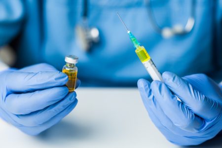 Foto mostra as mãos de um profissional da saúde em foco usando luvas e segurando uma seringa e uma ampola de vacina covid; pneumonia - Metrópoles