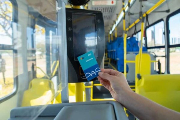 Foto colorida de mão estendida usando cartão passe livre estudantil em catraca de ônibus público