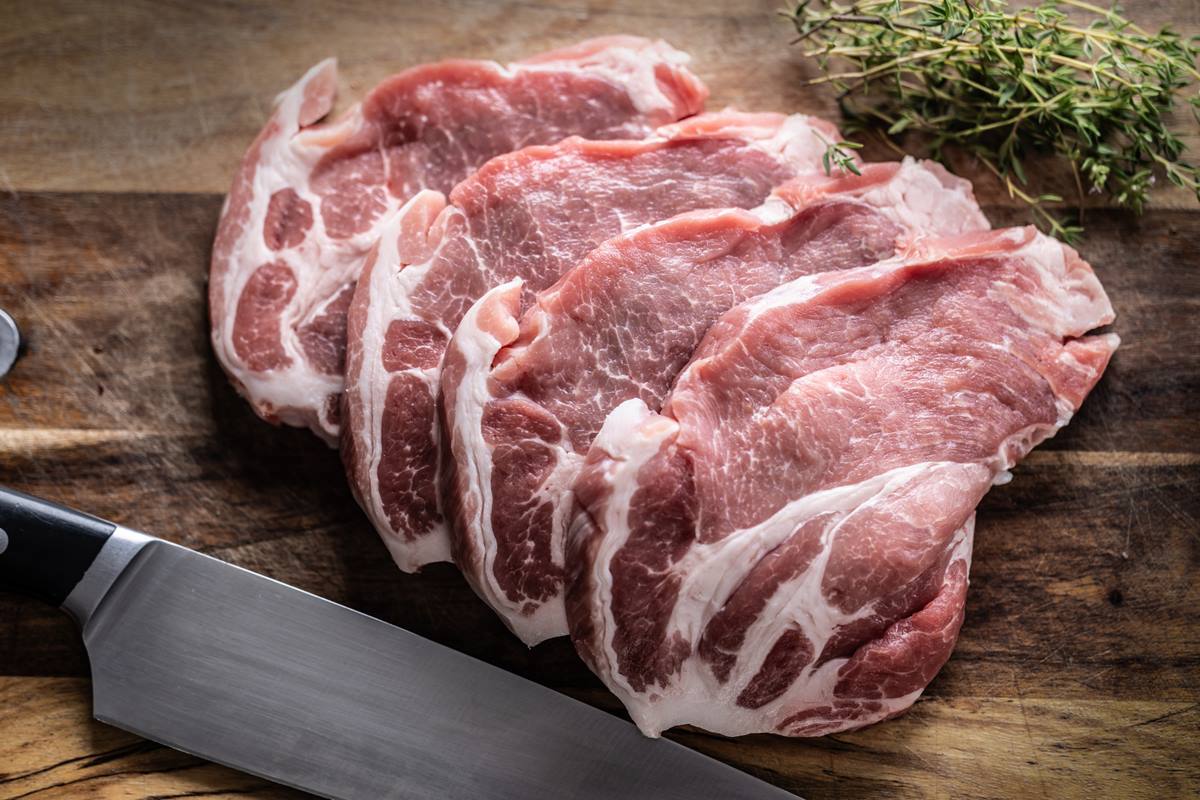 Foto colorida de fatias de carne de porco em uma tábua com tomilho - Metrópoles