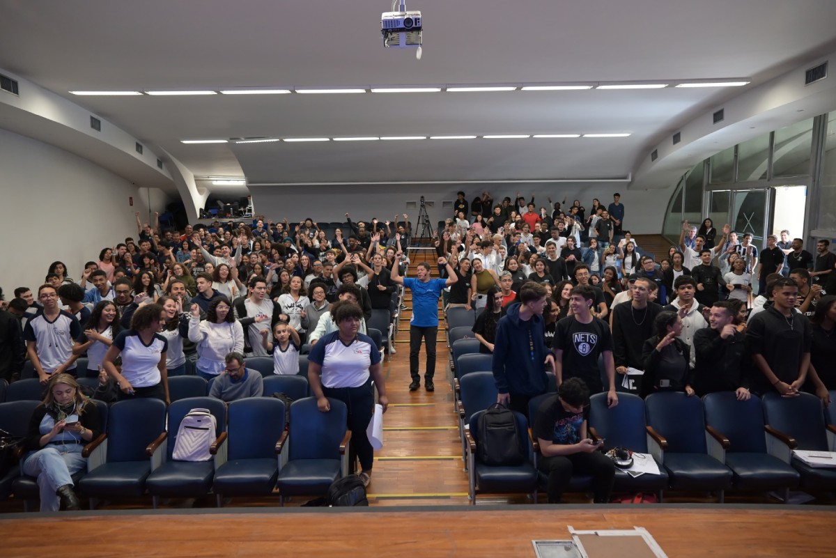 Fotografia colorida mostrando vários alunos em auditório com professor passando pelo corredor central-Metrópoles