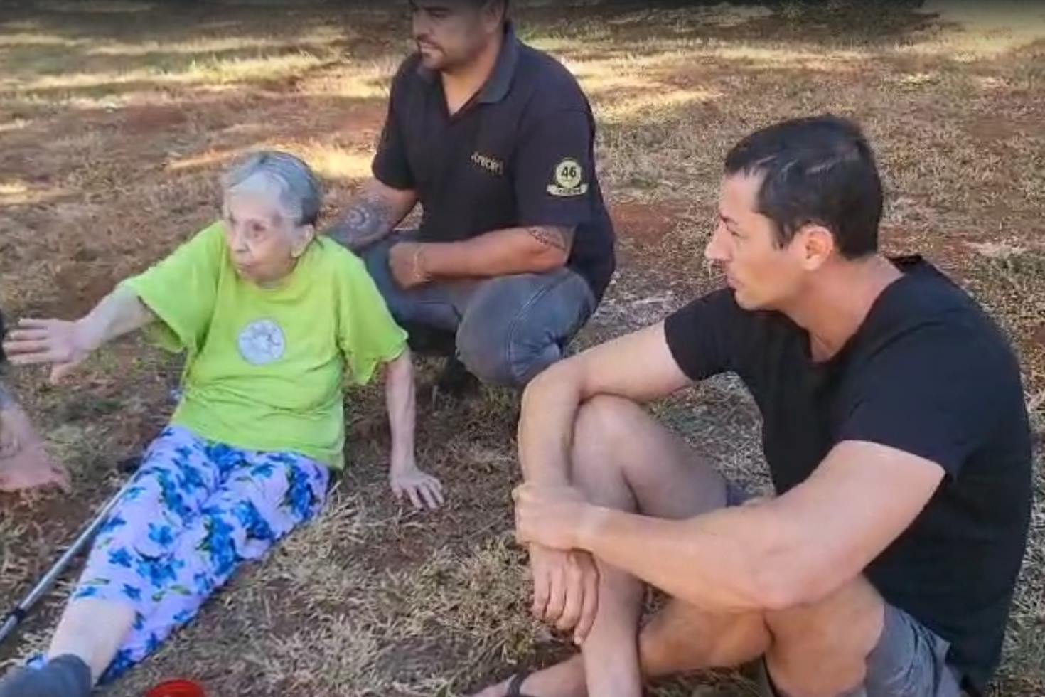 Imagem colorida de uma idosa, de camiseta verde e calça azul, sentada em um gramado