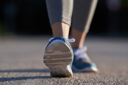 Foto em close-up mostra os tênis azuis de uma mulher durante caminhada. Metrópoles