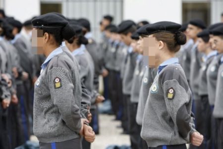 imagem colorida mostra pessoas vestidas com uniforme de escola militar, enfileiradas e com as mãos para trás - metrópoles