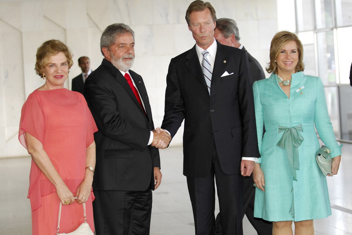 Foto colorida de homens de terno se cumprimentando ao lado de duas mulheres com roupas coloridas - Metrópoles
