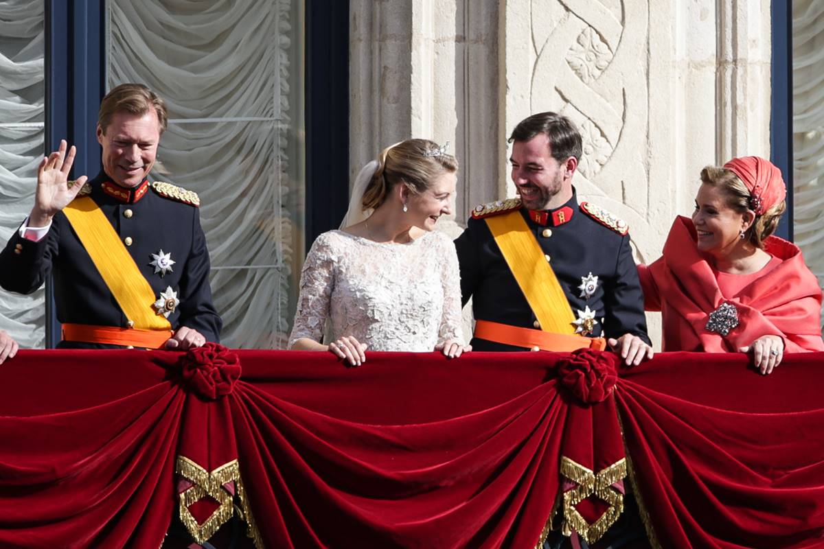 Foto colorida de dois homens e duas mulheres na varanda de um castelo. Eles estão conversando e uma mulher está com roupa de noiva - Metrópoles