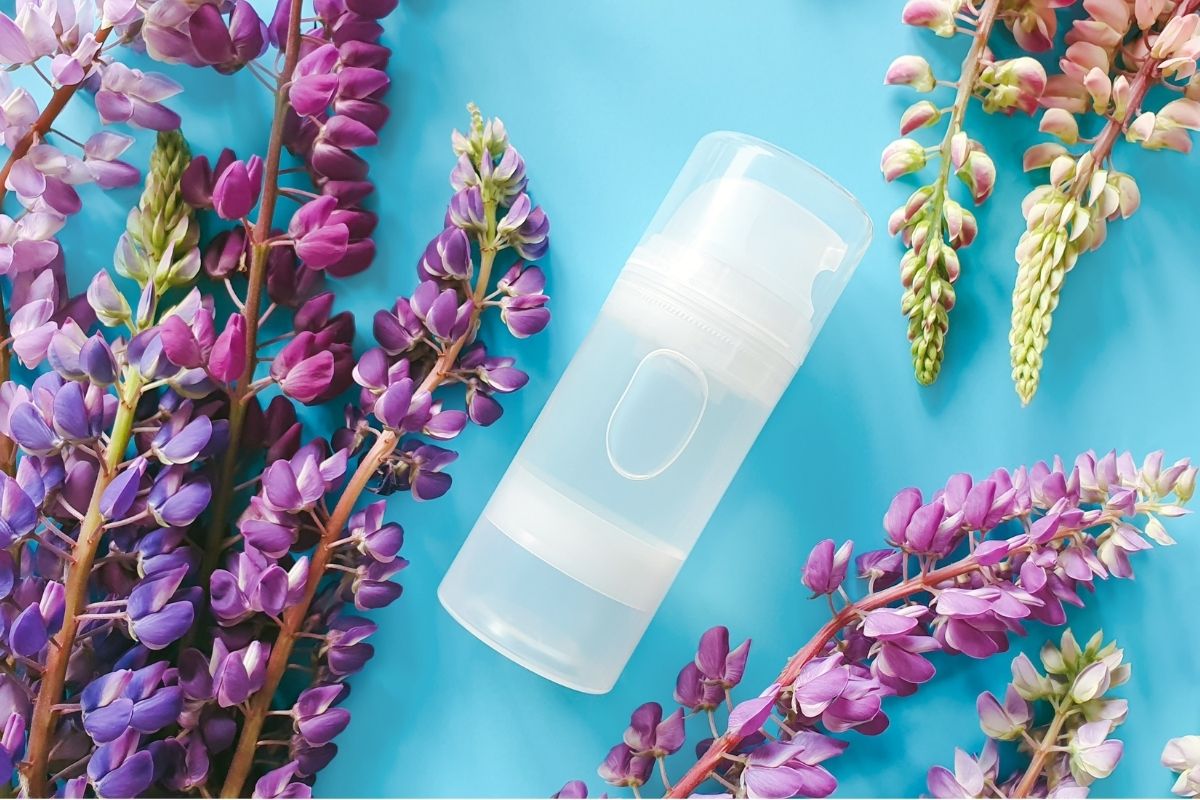 pote transparente de lubrificante em um fundo azul claro com flores roxas e rosas