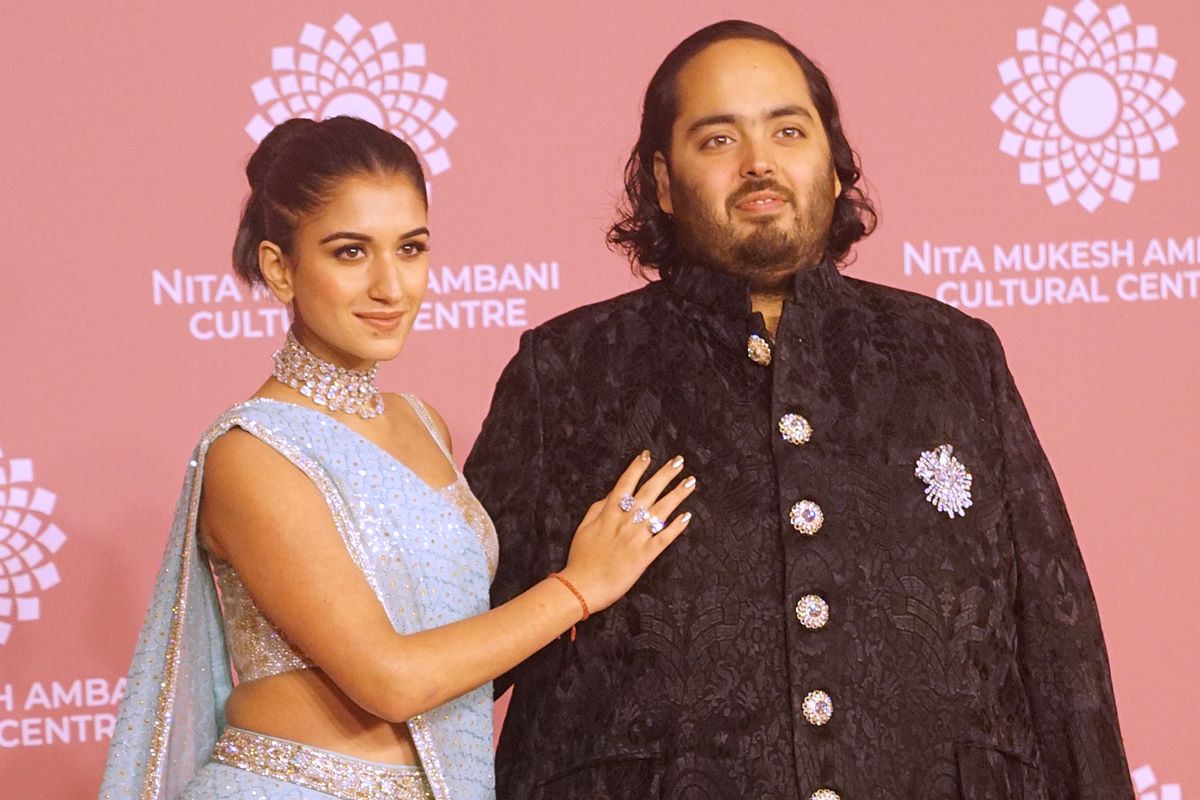 Foto colorida de mulher com saree azul ao lado de um homem com blusa preta - Metrópoles