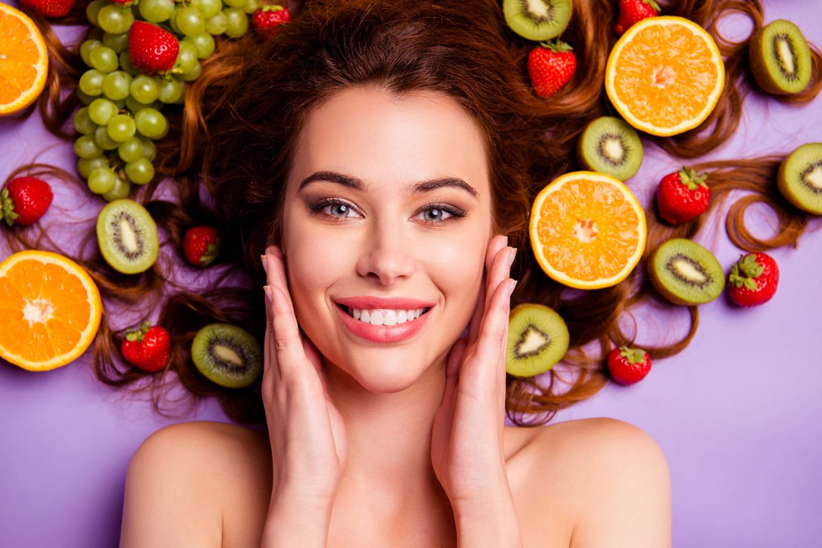 mulher sorrindo com as mãos no rosto em um fundo roxo com frutas