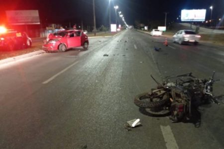 Foto colorida de carro vermelho e moto preta quebrados após acidente. Colisão de frente