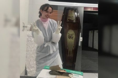 Imagem colorida de jovem uniformizada em frente a caixão