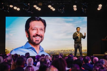 Imagem colorida mostra Ricardo Nunes falando em um palco, com uma imagem dele ao fundo projetada em um telão; evento foi boicotado por integrantes do União - Metrópoles