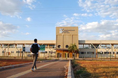 Foto colorida de predio do IFB Campus Taguatinga. Um estudante com uniforme da instituição e mochila nas costas anda até a entrada