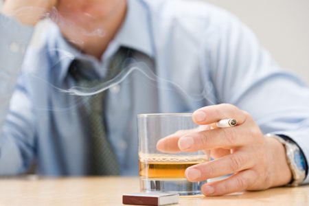 Homem de camisa social com cigarro e copo de bebida na mão - Metrópoles