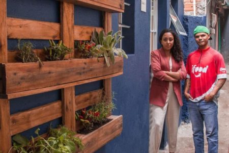 Mulher e homem em frente a uma parede azul com jardim externo