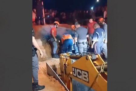 retroescavadeira cercada de bombeiros durante operação para salvar menino que caiu em buraco