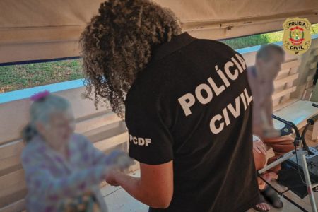 Foto colorida de mulher com uniforme da policia civil atendendo a idosa