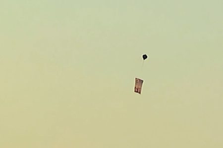 Imagem colorida de céu amanhecendo. É possível ver um balão com uma faixa pendurada abaixo - Metrópoles