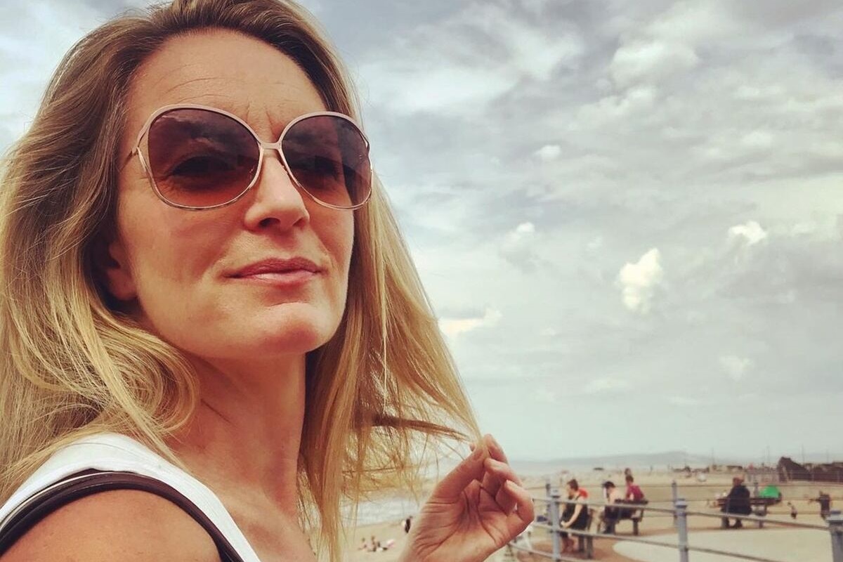 Beccy Barr posa, sorridente, de cabelos soltos e usando óculos escuros - Metrópoles