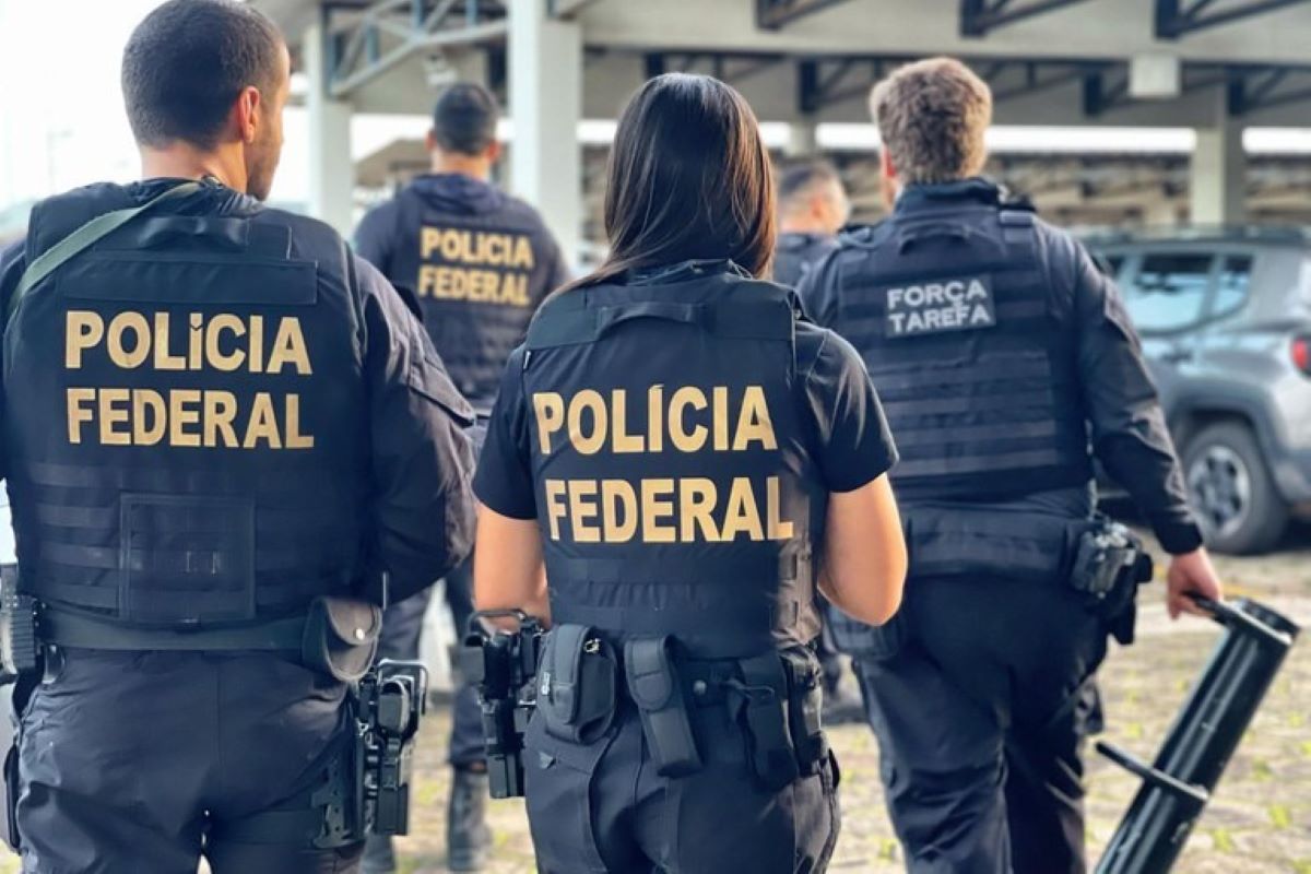 Imagem colorida mostra um homem e uma mulher, de costas, usando coletes pretos com as palavras "Polícia Federal" - Metrópoles
