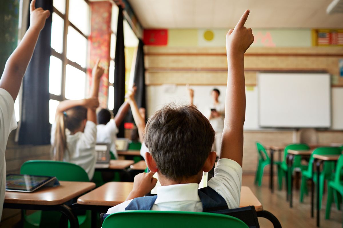 aluno, de costas, com a mão levantada em uma sala de aula crises climáticas