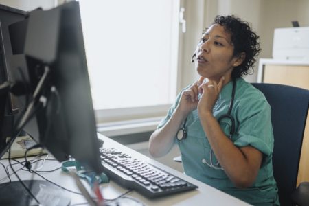 Jovem negra adulta em uma videochamada com paciente em casa. Conceito de telemedicina. Vista por cima do ombro. Teleconsulta. Telessaúde - Metrópoles