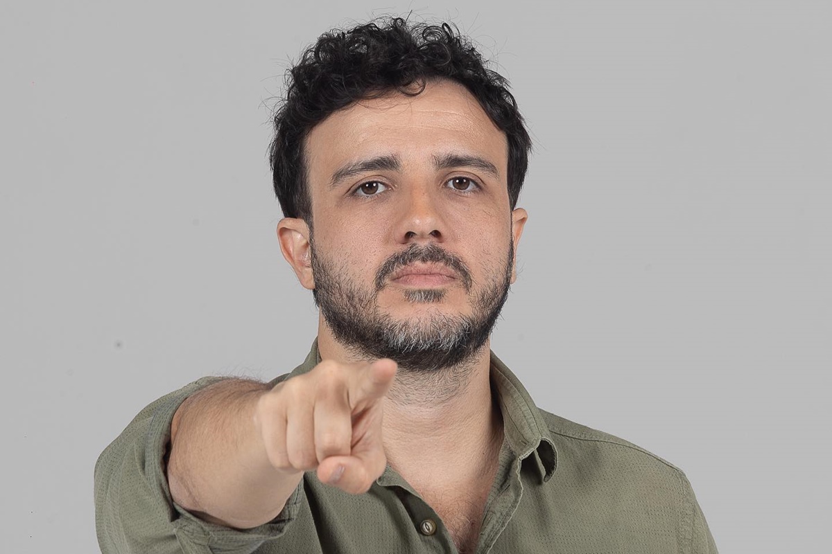 Imagem colorida traz uma foto feita em estúdio de Renan Santos, líder do MBL, dos ombros para cima. Renan é um homem branco, de cabelo castanho escuro e barba aparada escura. Ele veste uma camisa verde musgo e olha para a câmera sem sorrir. Seu braço direito está erguido e o dedo indicador da mão está apontando para a câmera - Metrópoles