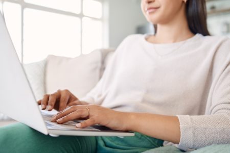 Foto de uma mulher usando seu laptop enquanto estava sentado no sofá em casa pesquisa sobre h1n1 - Metrópoles