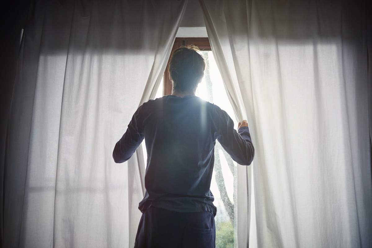 Foto de Homem abrindo cortinas no quarto - Metrópoles