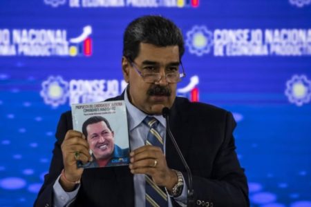 Foto colorida de Nicolás Maduro segurando um livro com foto do Hugo Chávez - Metrópoles