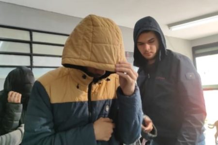 Imagem colorida de homem de cabeça abaixada, escondendo rosto com capuz de blusa - Metrópoles