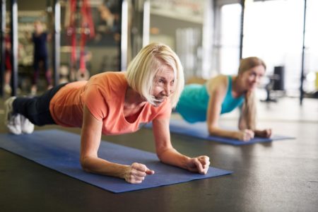 Mulher loira de meia idade e ativa fezendo exercícios para o abdômen, uma prancha no tapete durante treino no centro de fitness