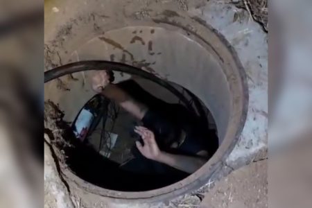 Imagem colorida de um homem dentro de um bueiro - Metrópoles