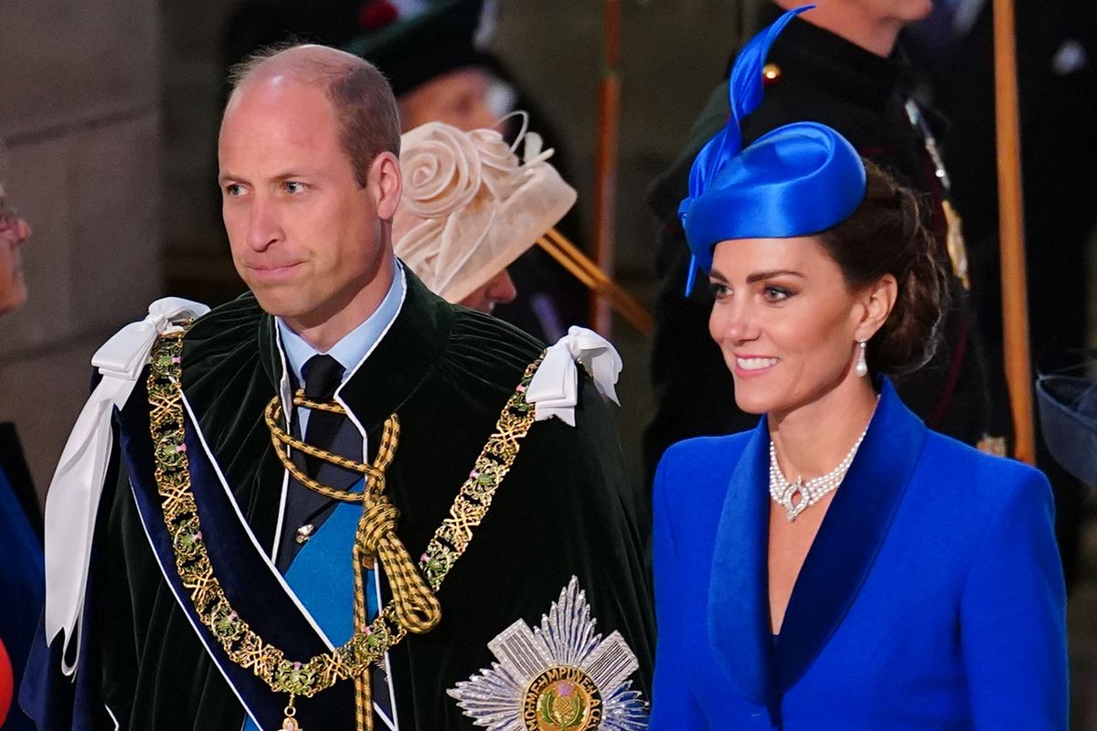 Foto colorida de homem com traje real ao lado de mulher com roupa e chapéu azul - Metrópoles