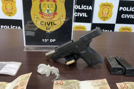 Foto colorida de arma de fogo e porção de cocaína em cima de mesa de apreensão da polícia civil