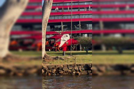 Imagem colorida de um helicóptero dos bombeiros pousado em um gramado em frente a um hotel