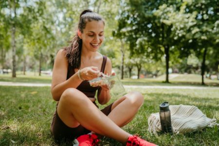 Foto colorida - mulher branca comendo no parque - dieta exercício físico