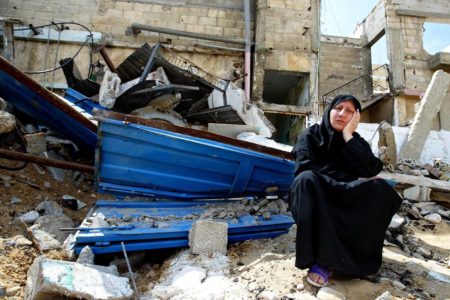 Imagem colorida mostra mulher palestina sentada em escombros na Faixa de Gaza - Metrópoles