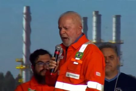 Imagem colorida do presidente Lula em discurso com jaqueta laranja da Petrobras - Metrópoles