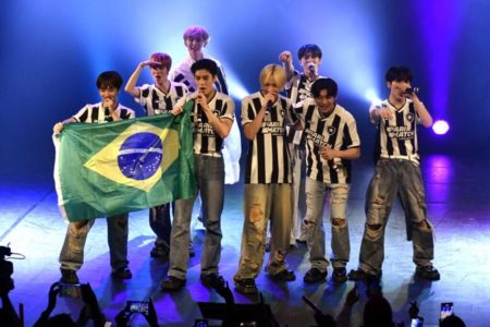 Imagem colorida mostra grupo de k-pop NTX. Eles seguram bandeira do Brasil e blusas listradas - Metrópoles