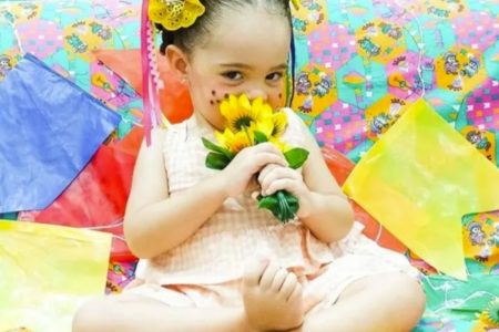 Menina cheira flor em cenário de festa junina - Metrópoles