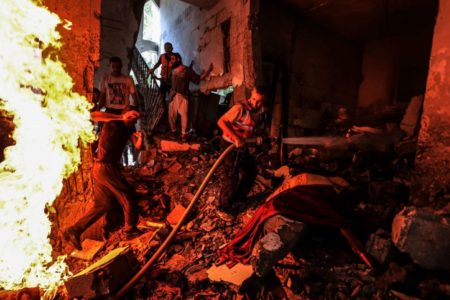 Imagem colorida de homens tentando apagar incêndio em construção na Faixa de Gaza - Metrópoles