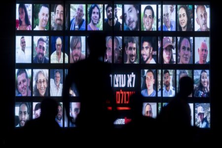 Pessoas passam por uma tela exibindo fotos de reféns sequestrados em 7 de outubro: seis corpos recuperados na Faixa de Gaza -- Metrópoles