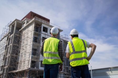 Imagem colorida de duas pessoas olhando para um prédio em construção - Metrópoles