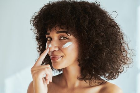 Foto colorida - mulher com cabelo cacheado usando protetor solar